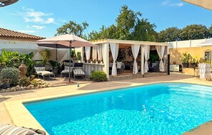 A swimming pool with a covered patio area, lounge chairs, and potted plants. - Maison avec piscine privée (Marguerittes)