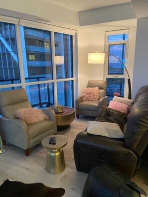 A modern living room with large windows, a sofa, armchairs, a coffee table, and a lamp.
