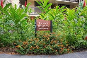 Schild mit der Aufschrift 'LAWAI BUILDING' und der Gebäudenummer 'L101 - L408' in einer begrünten Anlage mit Pflanzen und Blumen.