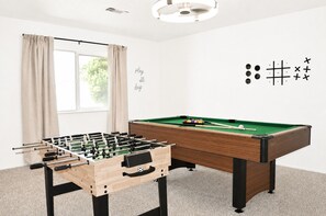 Um quarto com mesa de pebolim, mesa de bilhar e uma janela com cortinas.