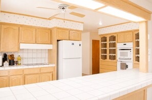 Eine Küche mit Holzausstattung, einem weißen Kühlschrank, einer Mikrowelle und einem Deckenventilator.