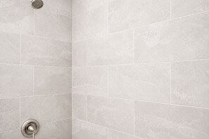 A corner of a tiled shower area with a showerhead and a control knob. - Modern 3BR Retreat + Game Room + 2 King Beds (Hanford)