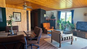 A cozy living room with wooden floors, a dining table, chairs, a sofa, a television, and a ceiling fan.