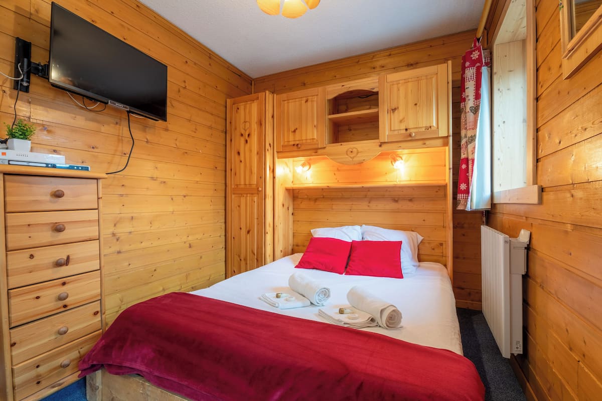 Una habitación con paneles de madera, una cama, un televisor y un aparador.