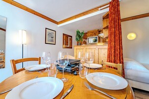 A dining area with a wooden table set for four, a television, and a kitchen area in the background.
