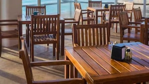 Uma sala de jantar com mesas e cadeiras de madeira, grandes janelas com vista para o mar.
