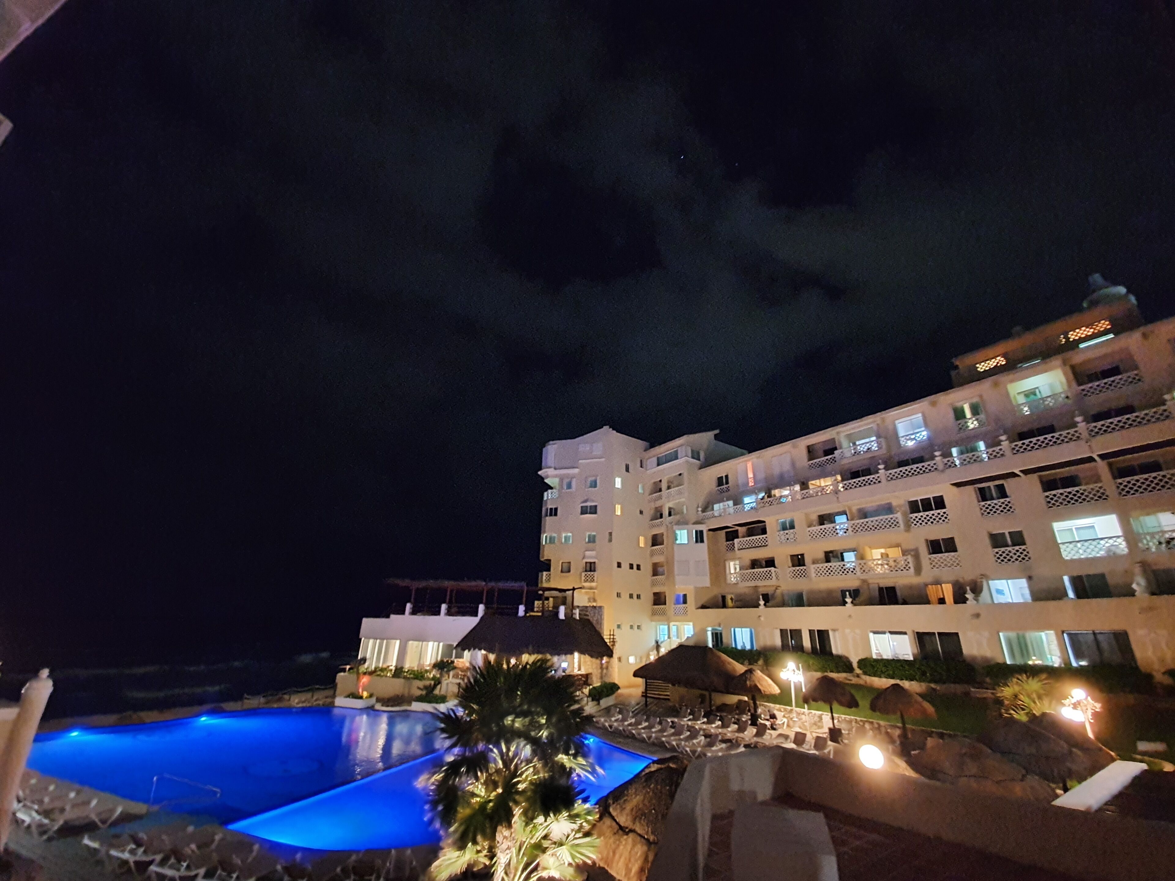 A hotel with a swimming pool, multiple balconies, and outdoor lighting.