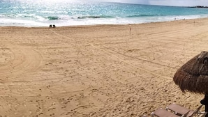 Uma praia com pegadas, um guarda-sol de palha e céu claro.