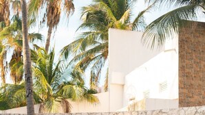 Paredes de pedra com placa 'CANCUN PLAZA', palmeiras e um edifício ao fundo.