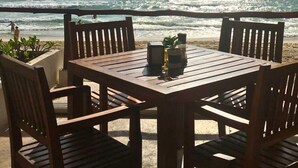 Uma mesa de madeira com cadeiras numa varanda com vista para o oceano.