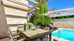 Ein Außenpoolbereich mit Tisch und Stühlen, einer Pergola und einer Steinmauer.