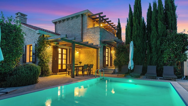 Ein Pool mit Pergola, Steinhaus und hohen Bäumen.