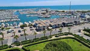A marina with numerous boats docked, a parking area, and a road with palm trees. - Paradis du Soleil by Interhome (La Grande Motte)
