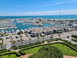 A marina with numerous boats docked, a parking area, and a road with palm trees. - Paradis du Soleil by Interhome (La Grande Motte)