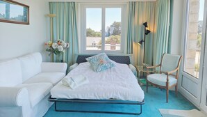 A bedroom with a bed, a white sofa, a chair, a floor lamp, and a window with curtains.