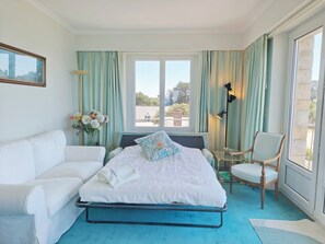A bedroom with a bed, a white sofa, a chair, a floor lamp, and a window with curtains.