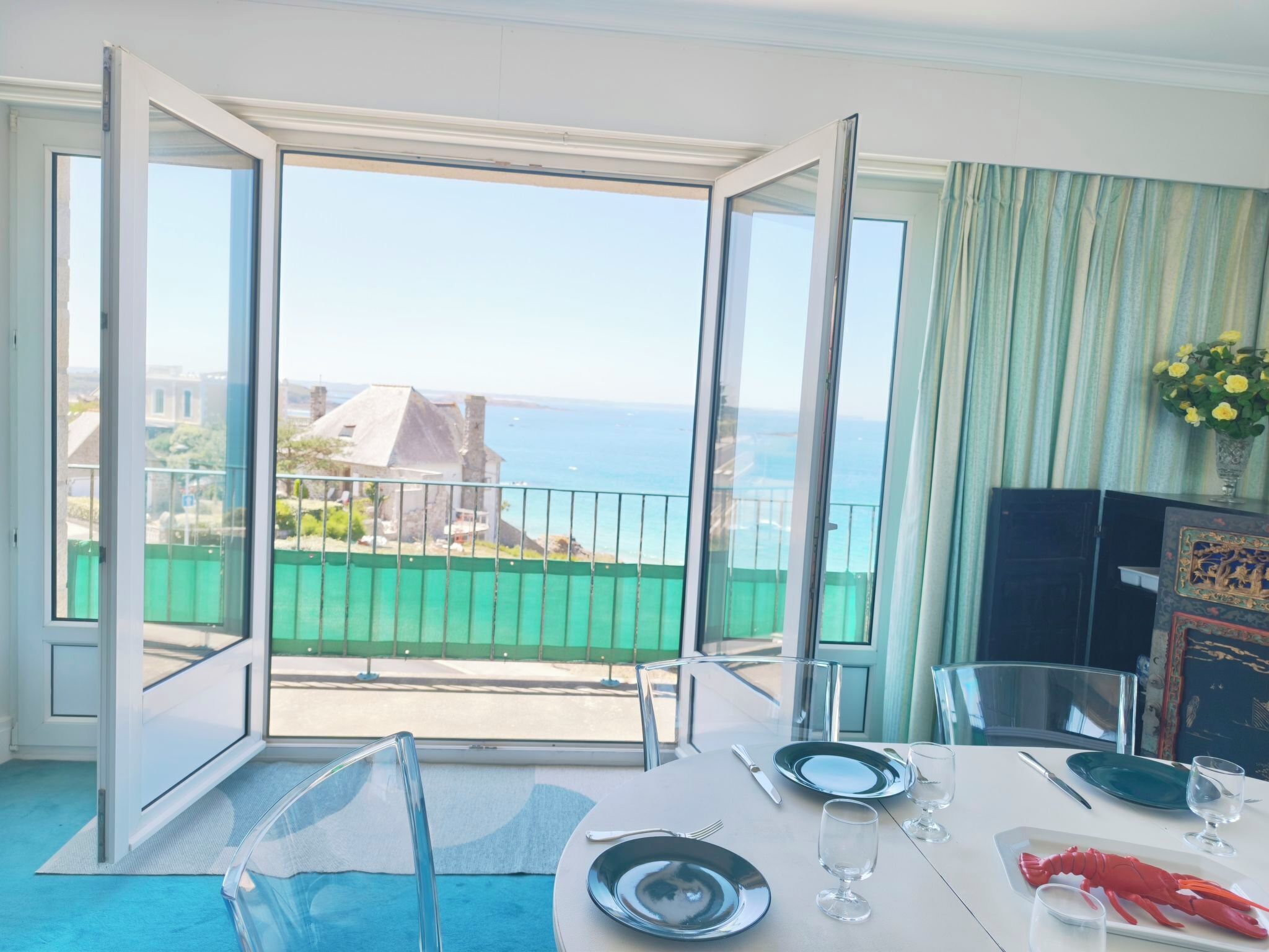 A dining area with a table set for two, a view of the sea, and a balcony with a railing.