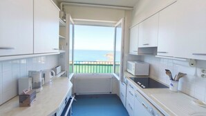 A compact kitchen with white cabinets, a microwave, a kettle, and a view of the sea through an open door.