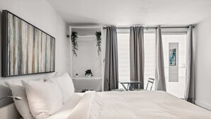 Une chambre moderne avec un grand lit, une table de chevet, une chaise, une petite table et une fenêtre avec des rideaux.