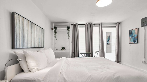 Une chambre moderne avec un grand lit, une table de chevet, une lampe, une chaise, un bureau et une fenêtre avec des rideaux.