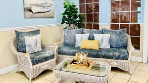 A room with two wicker sofas, a glass coffee table, a potted plant, and a painting of a boat on the wall. - The Jellyfish Resort-style (Galveston)