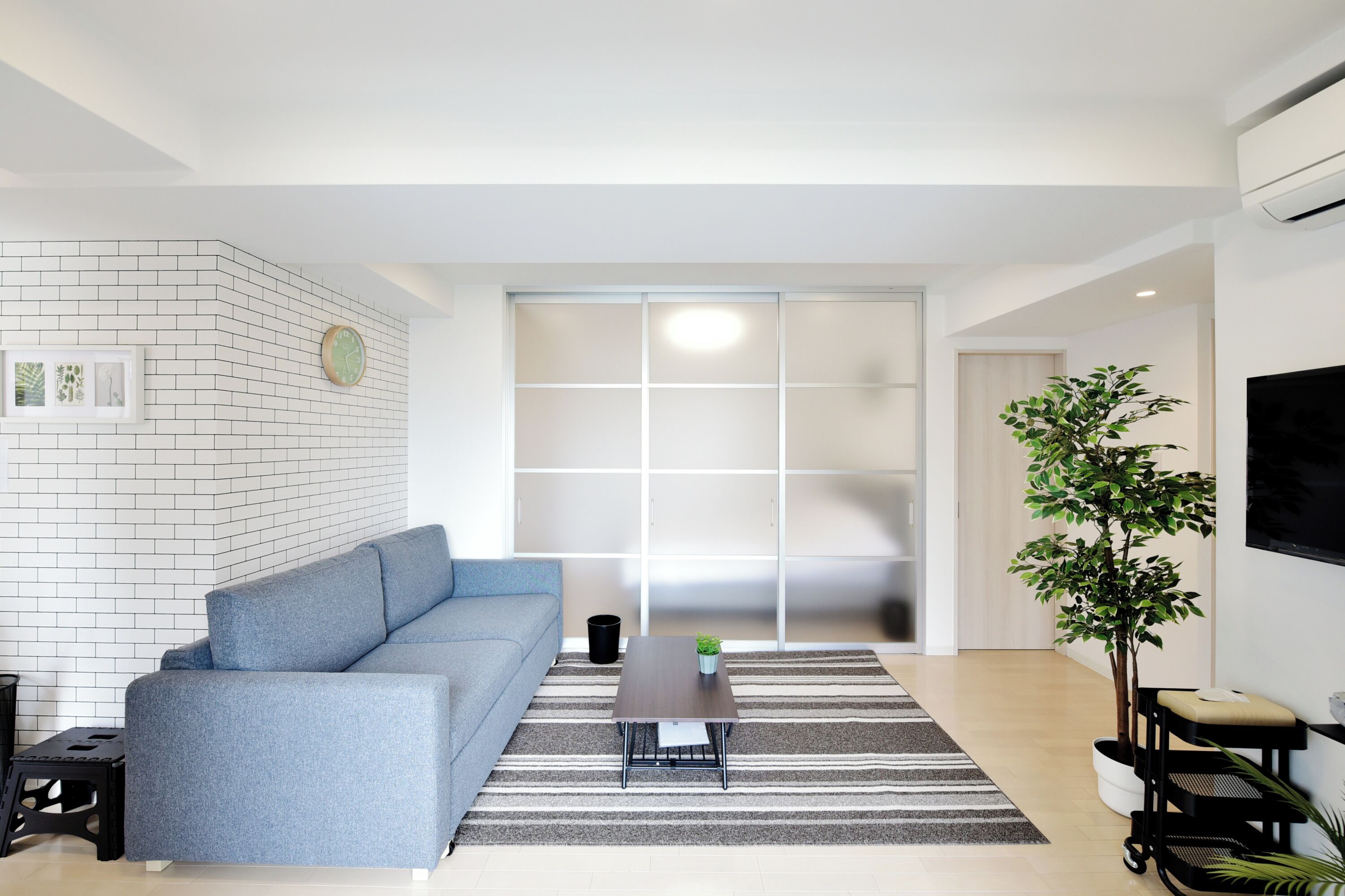A modern living room with a sofa, a coffee table, a TV, a plant, and a sliding door.
