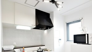 A compact kitchen with white cabinets, a black countertop, a microwave, a stove, and a ceiling fan. - 3 min to Honmachi Stn! Wi-Fi, Great Access to Namba, Umeda & Shinsaibashi (Kitakyuhouji-cho, Osaka City)