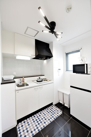 Eine kompakte Küche mit weißen Schränken, einer schwarzen Arbeitsplatte, einer Mikrowelle, einem Herd und einem Deckenventilator.