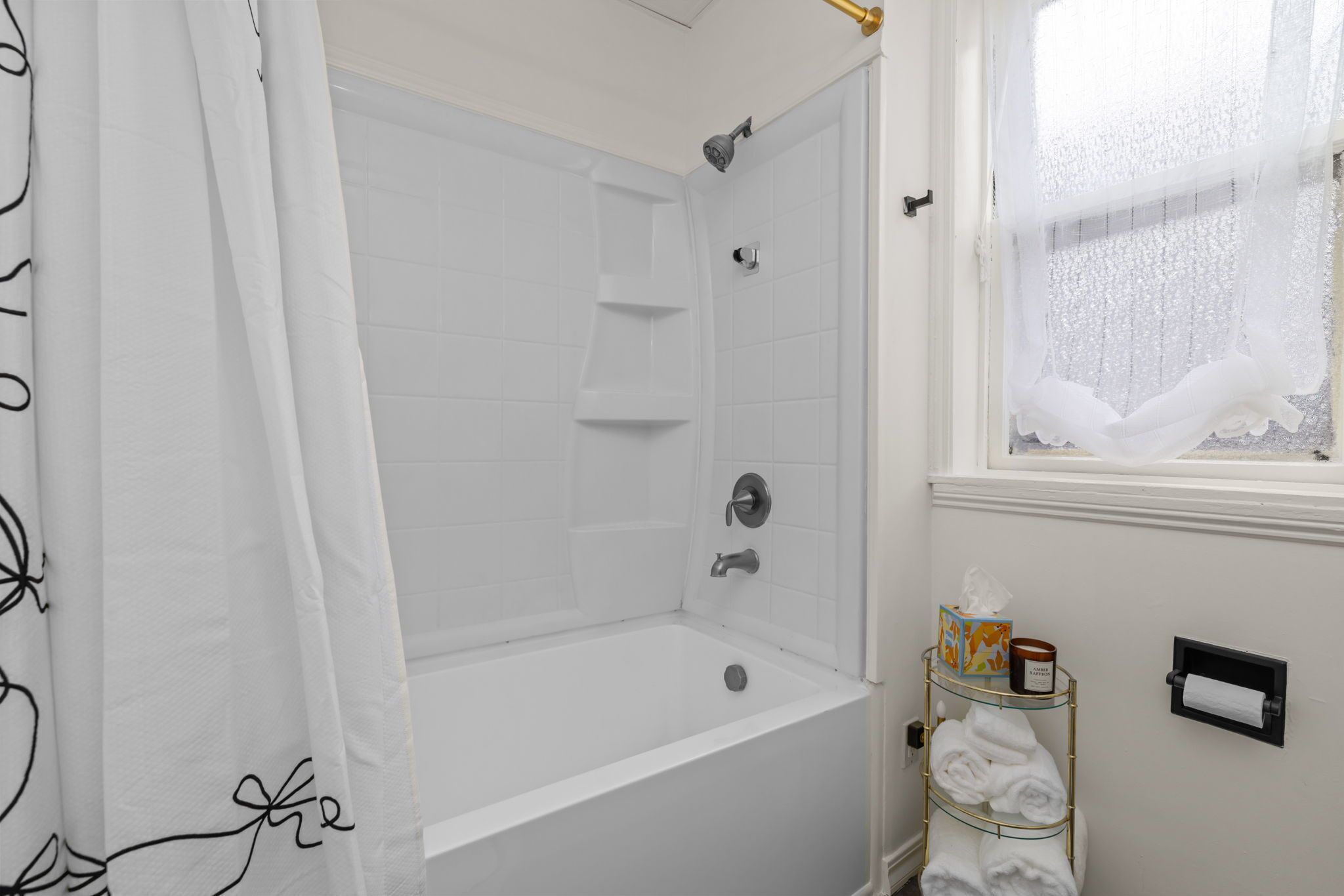 A bathroom with a bathtub, a shower, a window with a view, and a towel rack with towels.