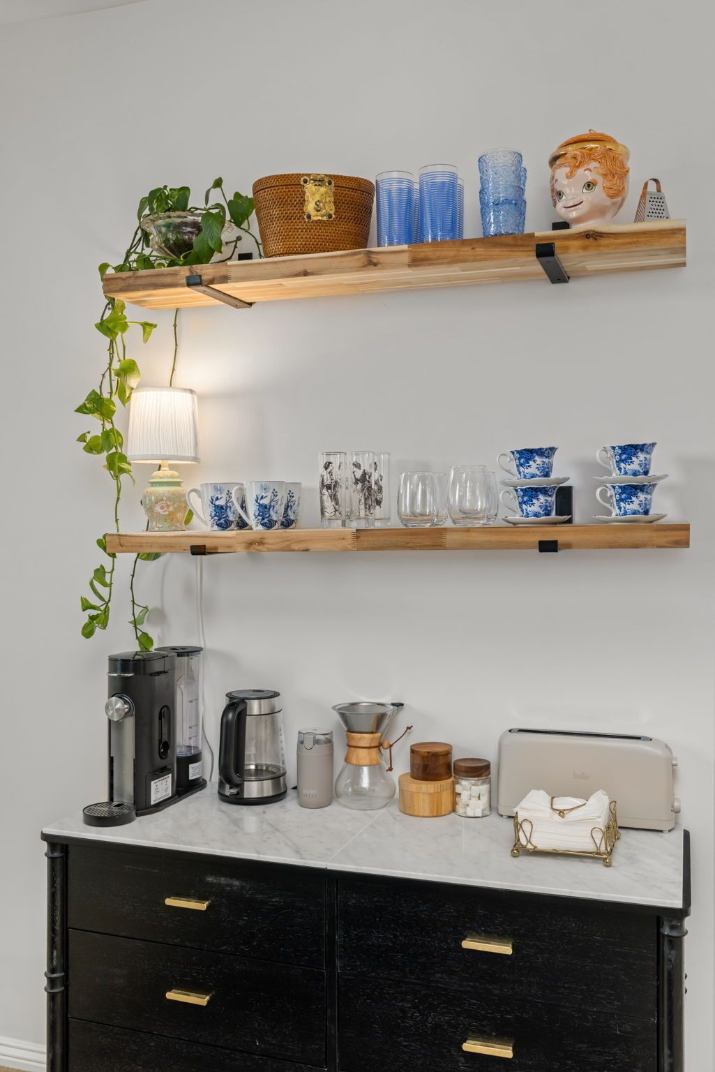 A kitchen with two wooden shelves, a coffee maker, a kettle, and a toaster.