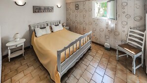 Une chambre à coucher comprenant un lit, une chaise, une table de chevet, une lampe, une fenêtre et un mur orné de motifs circulaires.