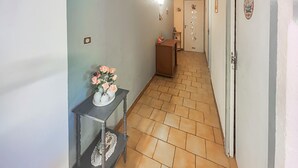 Un couloir doté d’un sol carrelé, une petite table ornée d’objets décoratifs et une porte avec un miroir.
