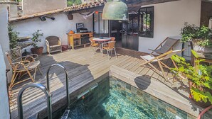 Uma área de piscina no terraço com deck de madeira, cadeiras de descanso e uma mesa.