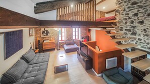 Uma sala de estar ampla com sofá, televisão, lareira e parede de pedra.
