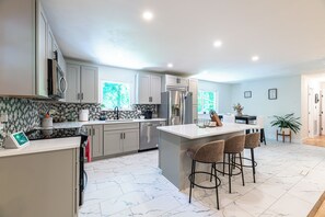Eine moderne Küche mit einer zentralen Kochinsel, Barhocker und einem Essbereich mit Tisch und Stühlen.