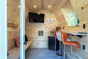 Ein gemütliches Blockhaus-Interieur mit Holzvertäfelung, einem an der Wand befestigten Fernseher, einer Bar mit Hockern und einem Fenster mit Blick.