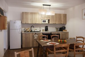 A compact kitchen with wooden cabinets, a white refrigerator, a microwave, and a dining table with chairs. - Au Logis Noisette - SAINT LOUP GEANGES (SAINT LOUP GEANGES)
