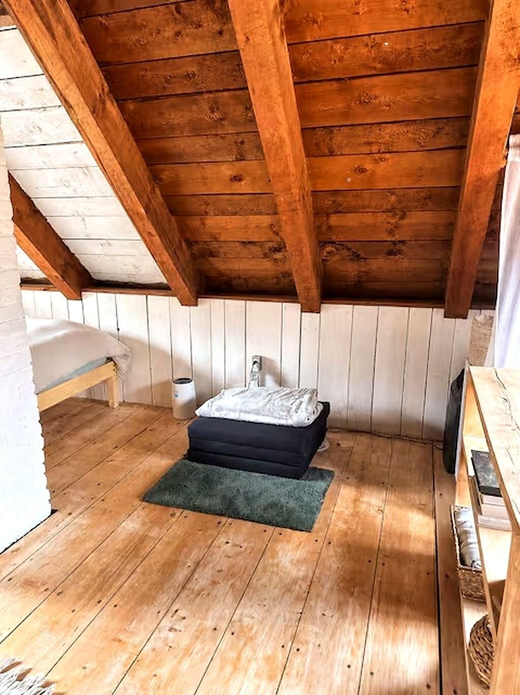 Un dormitorio acogedor en el ático, con vigas de madera, un banco, una mesita de noche y una alfombra.