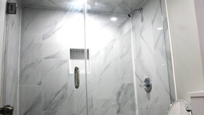 A bathroom with a glass-enclosed shower, a toilet, and a mirror.