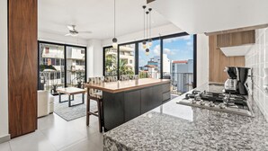 A modern kitchen with a large island, a dining area with a table and chairs, and a view of the outside. - Villa Borghese Roma · Condo in Trendy Versailles (Puerto Vallarta)