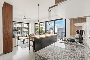 A modern kitchen with a large island, a dining area with a table and chairs, and a view of the outside. - Villa Borghese Roma · Condo in Trendy Versailles (Puerto Vallarta)