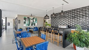 A modern restaurant with blue chairs, wooden tables, a black bar, and a geometric wall pattern. - Villa Borghese Roma · Condo in Trendy Versailles (Puerto Vallarta)