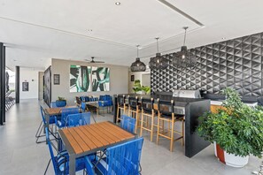 A modern restaurant with blue chairs, wooden tables, a black bar, and a geometric wall pattern. - Villa Borghese Roma · Condo in Trendy Versailles (Puerto Vallarta)