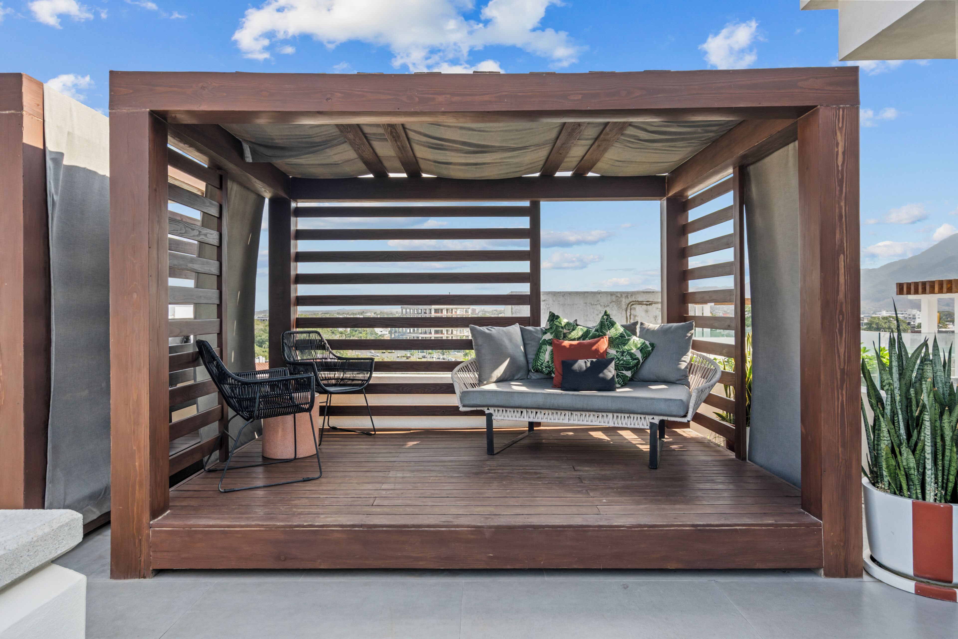 A wooden deck with a sofa and chairs, a potted plant, and a view of the city.