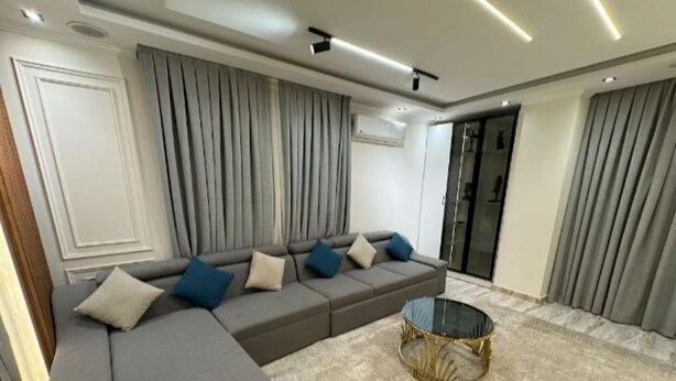 Ein modernes Wohnzimmer mit einer Eckcouch, einem runden Couchtisch und einem großen Fenster mit Vorhängen.