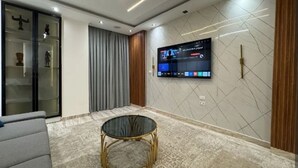 Ein modernes Wohnzimmer mit einem flachbildfernseher an der Wand, einem runden Glastisch und einem grauen Sofa.