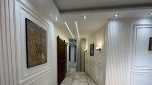 Ein Flur mit weißen Wandpaneelen, einem Marmorboden, eingelassener Beleuchtung und einer Karte im Bilderrahmen an der linken Wand.