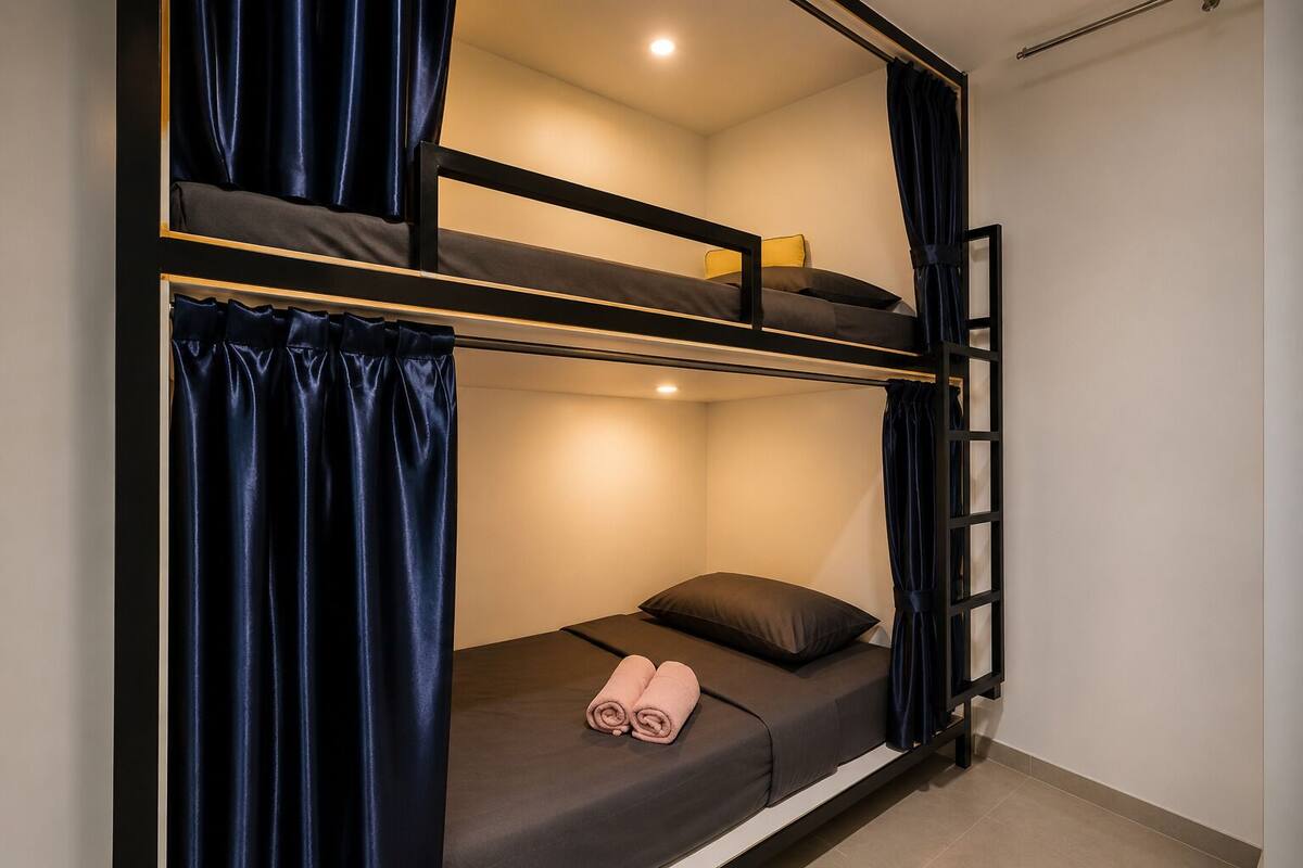 Ein Etagenbett mit einer Leiter, ein Einzelbett mit einem Kopfkissen und ein zusammengerolltes Handtuch auf der unteren Etage.