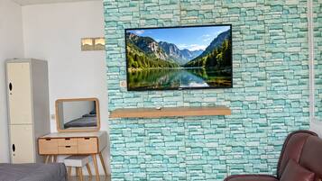 Un dormitorio con pared de diseño de piedra, un televisor montado, una cama, un escritorio con silla y un sofá de cuero marrón.
