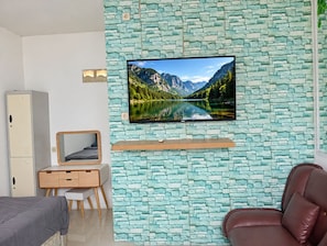 A bedroom with a stone-patterned wall, a mounted TV, a bed, a desk with a chair, and a brown leather sofa.